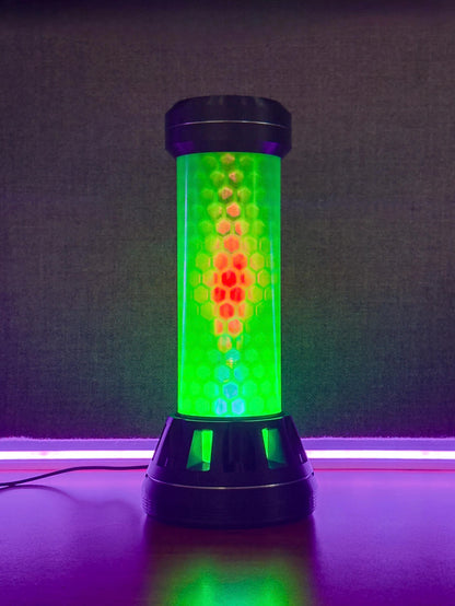A cylindrical LED light fixture with a black base and top, featuring a glowing green and red honeycomb pattern on a dark textured background.