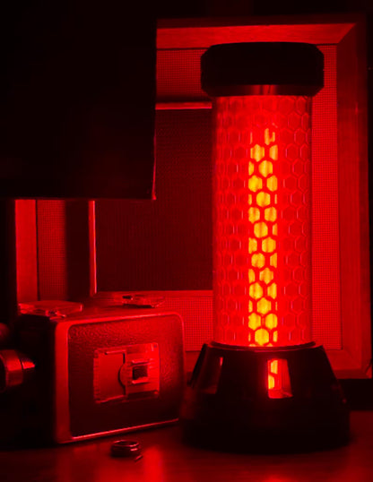 A red cylindrical lamp or light fixture with a honeycomb pattern on its body, glowing with a warm orange-red light, shown in a dark room next to a vintage camera.